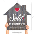 A realtor holding a wooden house-shaped sign that says Sold By during a client closing.