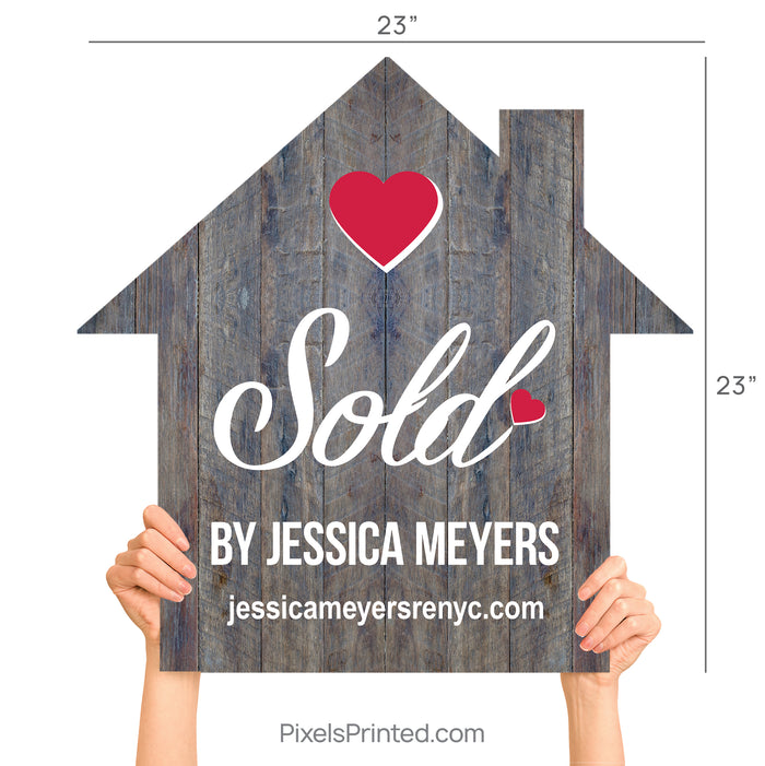 A realtor holding a wooden house-shaped sign that says Sold By during a client closing.