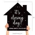 Realtor and client standing at a title company holding an It's Closing Day house-shaped sign.